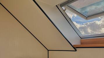 A bedroom with a sloped ceiling, a skylight, a bed with white bedding, and a wooden headboard.