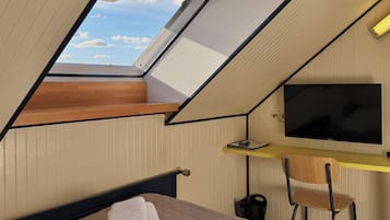 Una habitación con cama, un escritorio con silla, televisión y tragaluz.