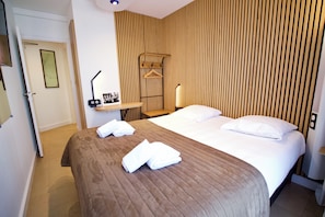 Habitación de hotel con una cama grande, dos almohadas, una mesita de noche con lámpara y una pared de listones de madera.