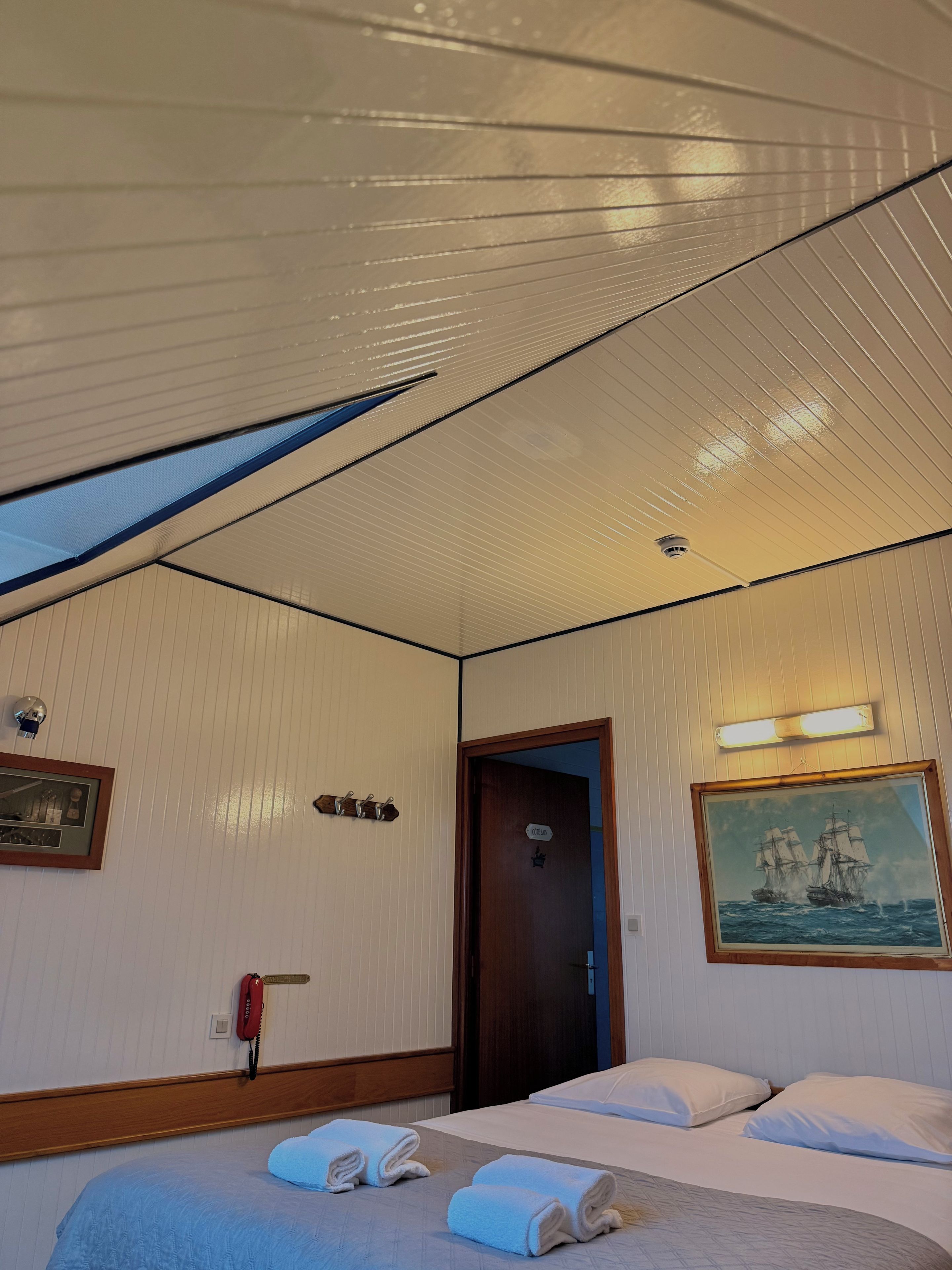 A hotel room with a bed, a painting, a door, and a phone.