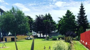 A well-maintained grassy area with a variety of plants and trees, a red wall, and a building in the background. - Le Voltaire (Rennes)