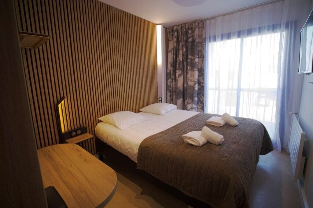 A hotel room with a bed, a bedside table, a lamp, and a window with curtains.