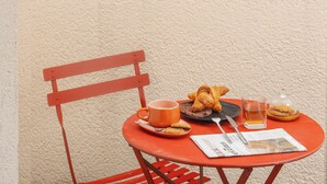 Una silla roja y una mesa con desayuno en un balcón con vistas a la ciudad.