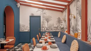 Un restaurante con una barra larga, sillas naranjas y un mural de flora del desierto en la pared.