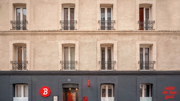 Un edificio con varias ventanas, una puerta y un letrero que indica un hotel. Hay dos macetas con plantas frente a la entrada.