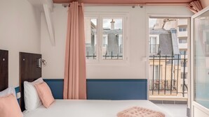 Un dormitorio con cama, ventana y vista a edificios.