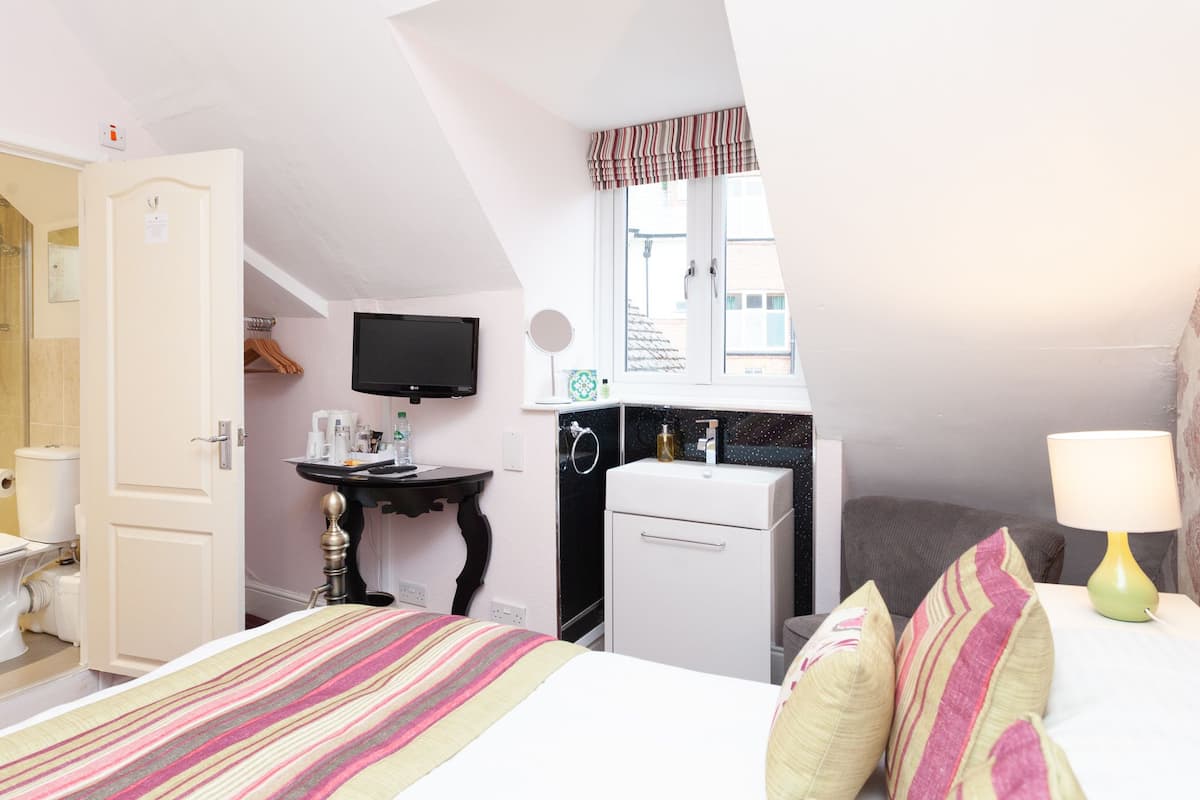 A hotel room with a bed, a desk, a television, a small kitchenette, and a window.