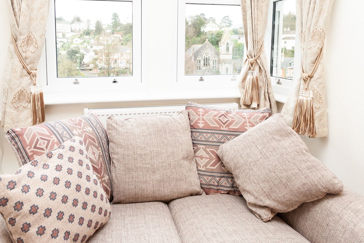 A cozy seating area with patterned cushions and a view of a church through a window.
