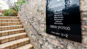 A black sign with white text for Ravenswood Bed and Breakfast, including a phone number and multilingual welcome message. - The Ravenswood B&B (Torquay)
