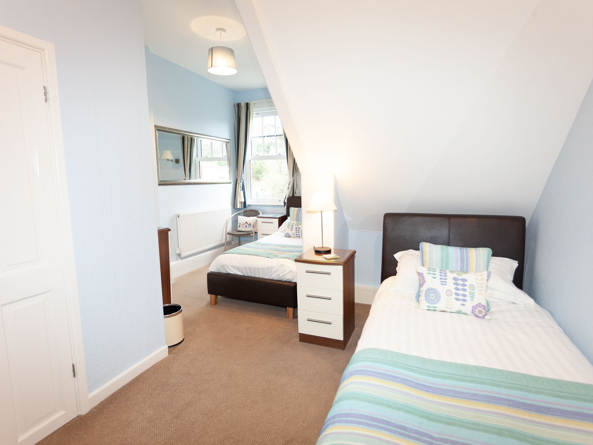 Quarto com cama, mesa de cabeceira, uma cadeira e uma janela.