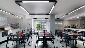 A modern dining area with tables and chairs, a counter with a coffee machine, and artwork on the walls. - Hotel Albatros (Gandia)