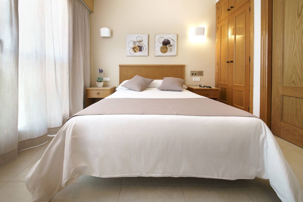 A neatly made bed with a wooden headboard, a bedside table with a lamp, and a large wardrobe.