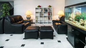 A modern living room with leather sofas, a white bookshelf, and a fish tank. - Hotel Albatros (Gandia)