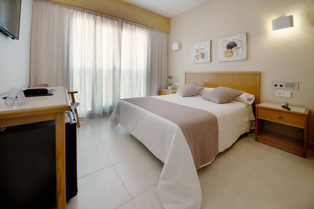 A hotel room with a bed, bedside tables, a desk, a chair, and a TV.