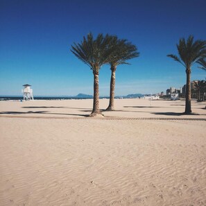 A sandy beach with palm trees and a lifeguard tower in the background. - Hotel Albatros (Gandia)