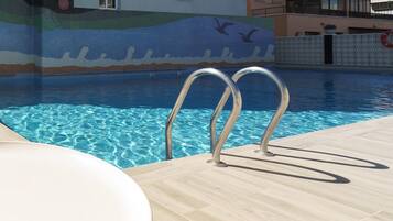 Una piscina con agua azul cristalina, un mural de azulejos con criaturas marinas y un flotador en la pared.