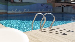 Una piscina al aire libre, sombrillas, sillones reclinables de piscina