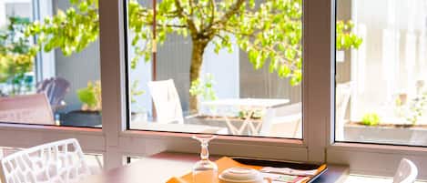 A table with a tray containing a glass, a mug, and some papers, set against a window with a view of a tree and outdoor furniture.