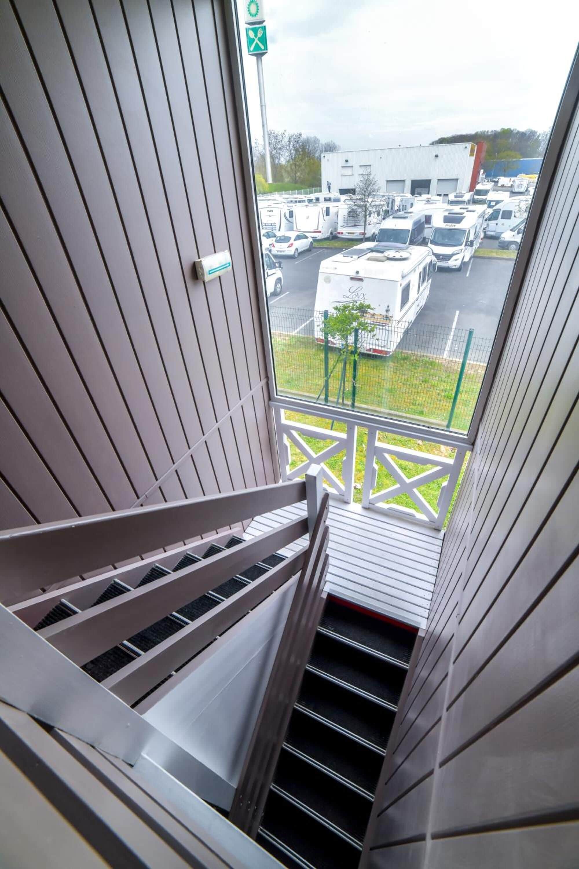 A view from a window overlooking a parking lot with RVs and a building in the background.