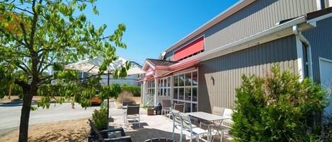 An outdoor seating area with tables and chairs, a covered patio, and a building with a red awning.
