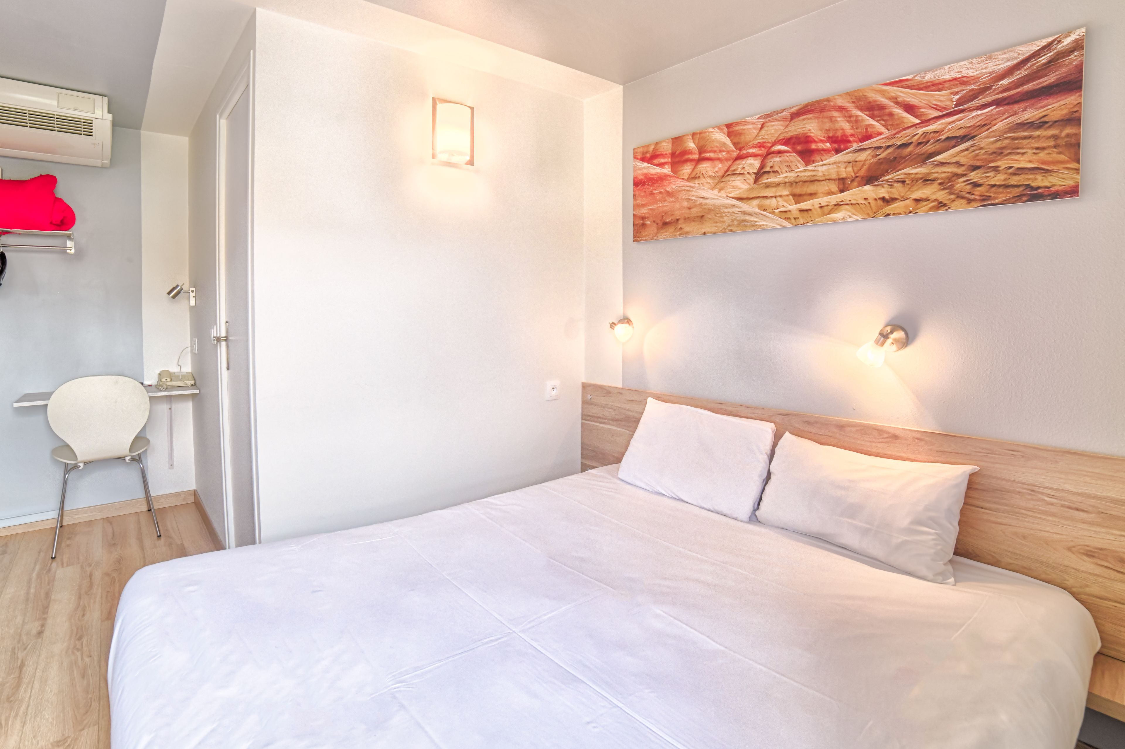 A modern hotel room with a large bed, a wooden headboard, and a wall-mounted artwork.