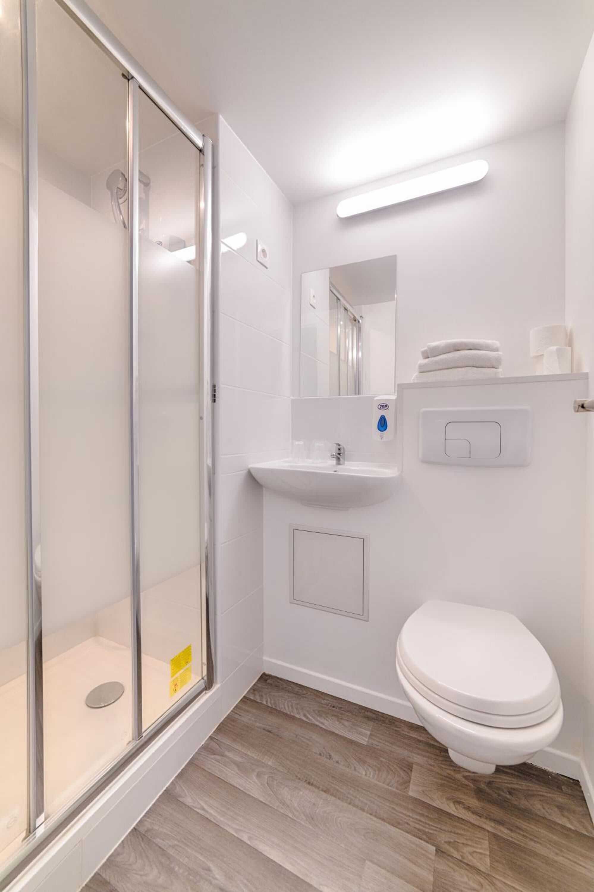 Un baño moderno con cabina de ducha de vidrio, un lavabo blanco y un inodoro.