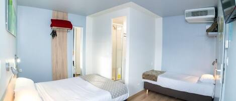 Una habitación de hotel compacta con dos camas individuales, un escritorio pequeño y un vestidor.