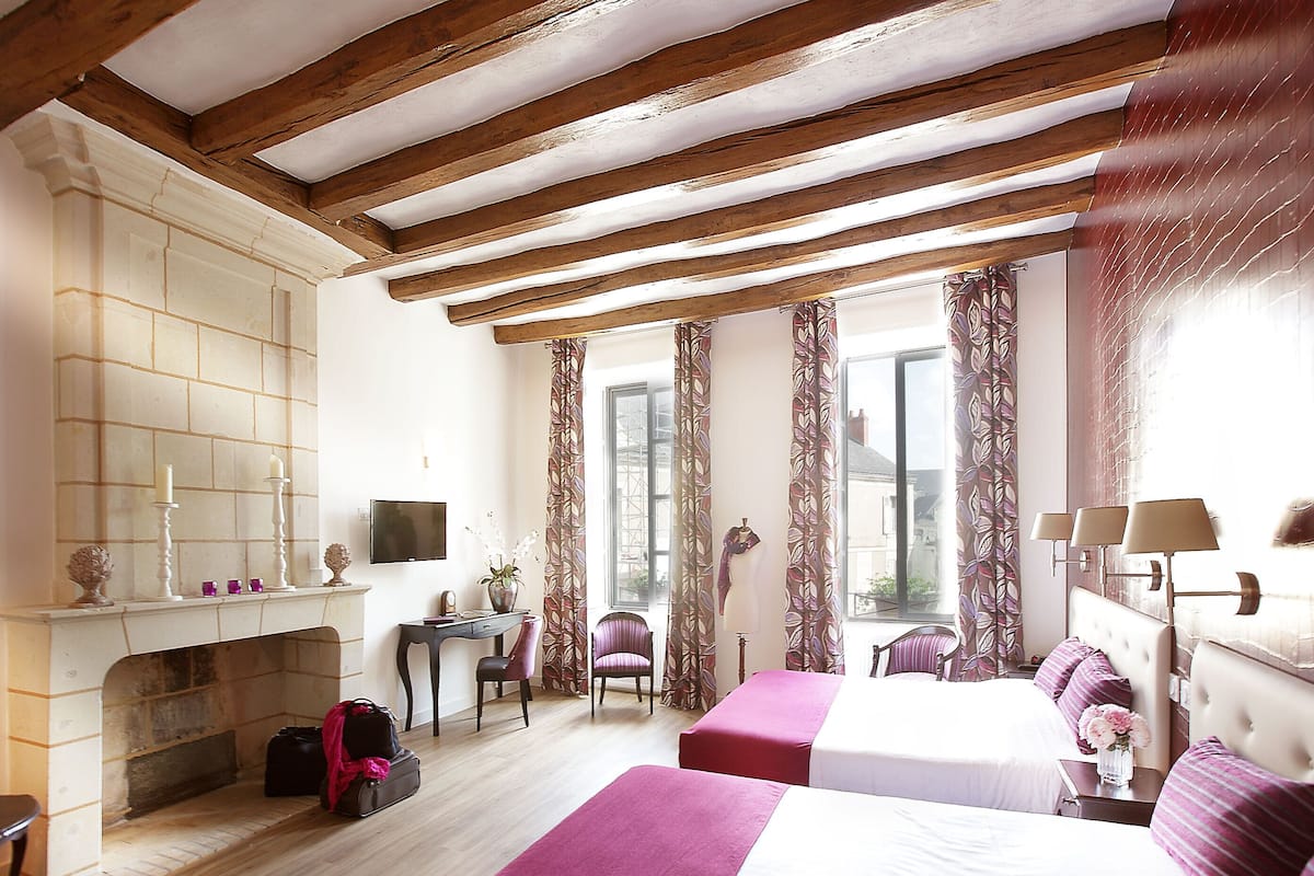 A hotel room with a fireplace, two beds, a desk, and a chair.