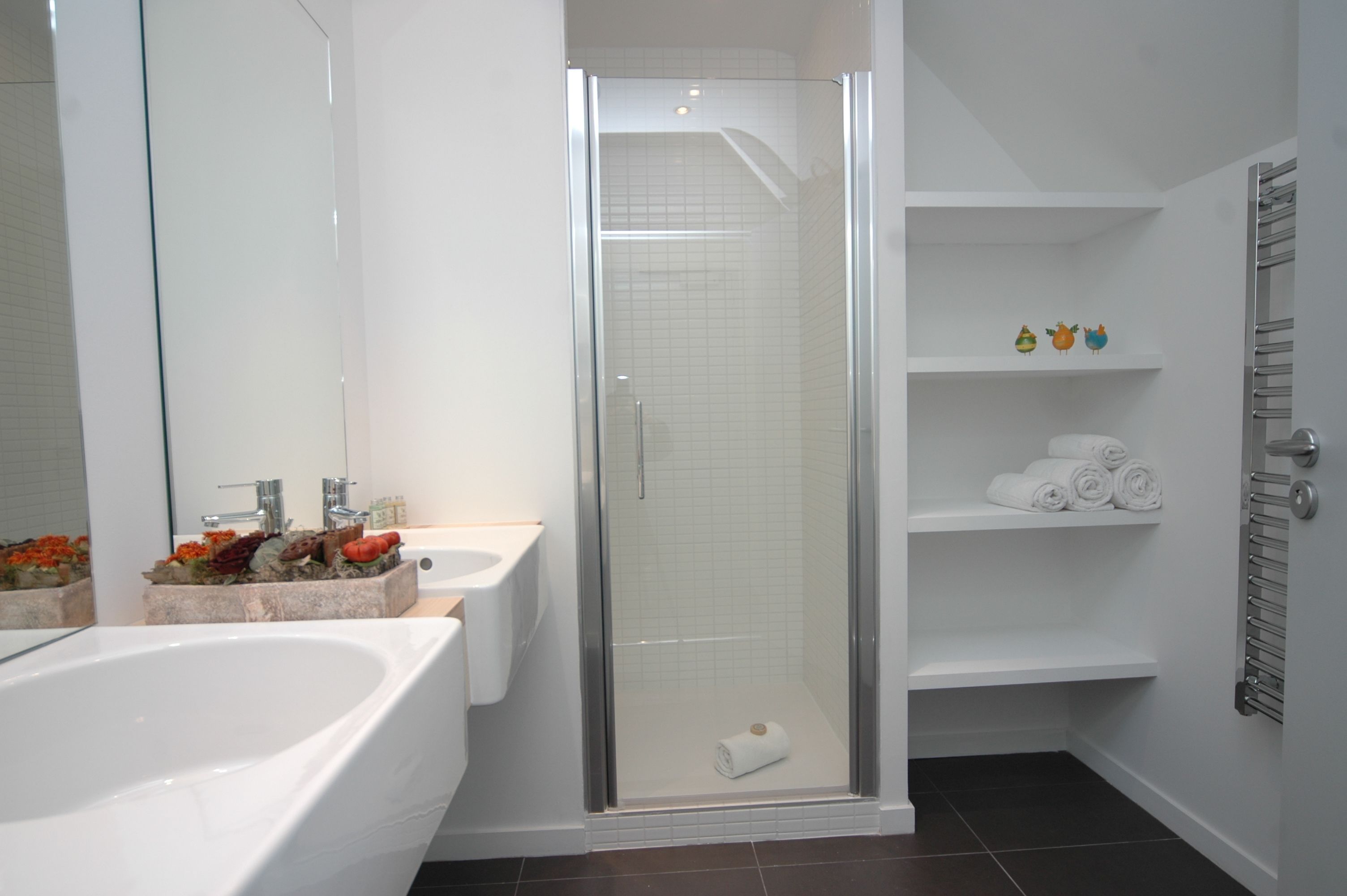 A modern bathroom with a glass-enclosed shower, a double sink, and a built-in shelf with towels.