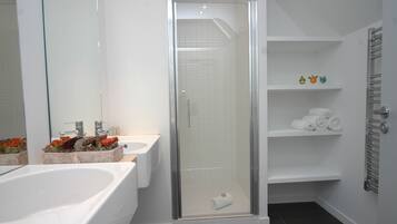 A modern bathroom with a glass-enclosed shower, a double sink, and a built-in shelf with towels.