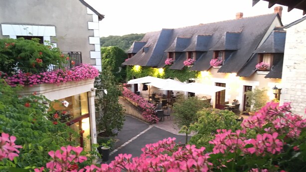 A courtyard with a stone building, a covered seating area, and pink flowering plants. - Hostellerie La Croix Blanche (Fontevraud-l'Abbaye)