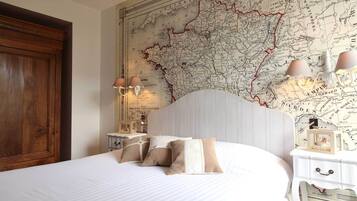 Un dormitorio con un mapa grande en la pared, un armario de madera, una mesita de noche blanca con lámparas y una cama con ropa de cama a rayas.