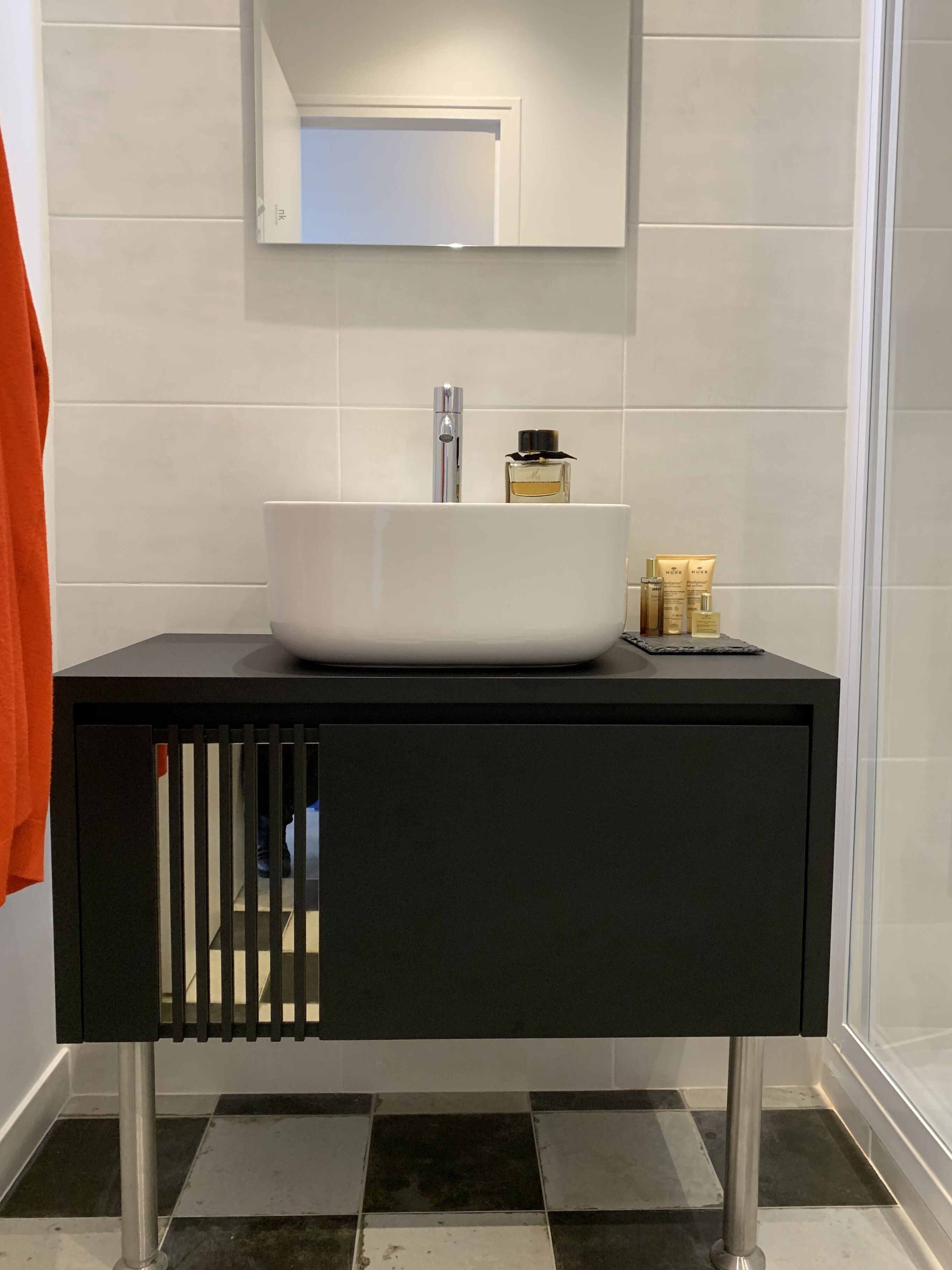 A modern bathroom with a white sink, a mirror above it, and a black cabinet below.