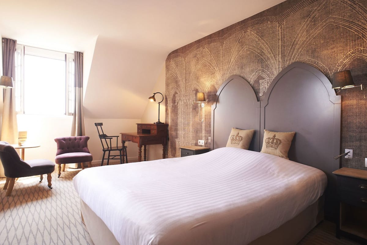 A hotel room with a large bed, a desk, two chairs, and a patterned wall.