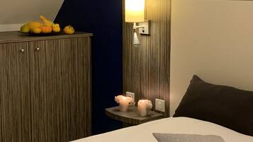 A hotel room with a bed, a nightstand with a lamp, a wooden headboard, and a wall-mounted shelf with decorative items.