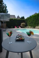 A poolside setting with two martini glasses, a tray of snacks, and a patio umbrella.