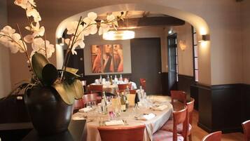 Un restaurante con una larga mesa dispuesta para comer, un jarrón grande con orquídeas y obras de arte en la pared.