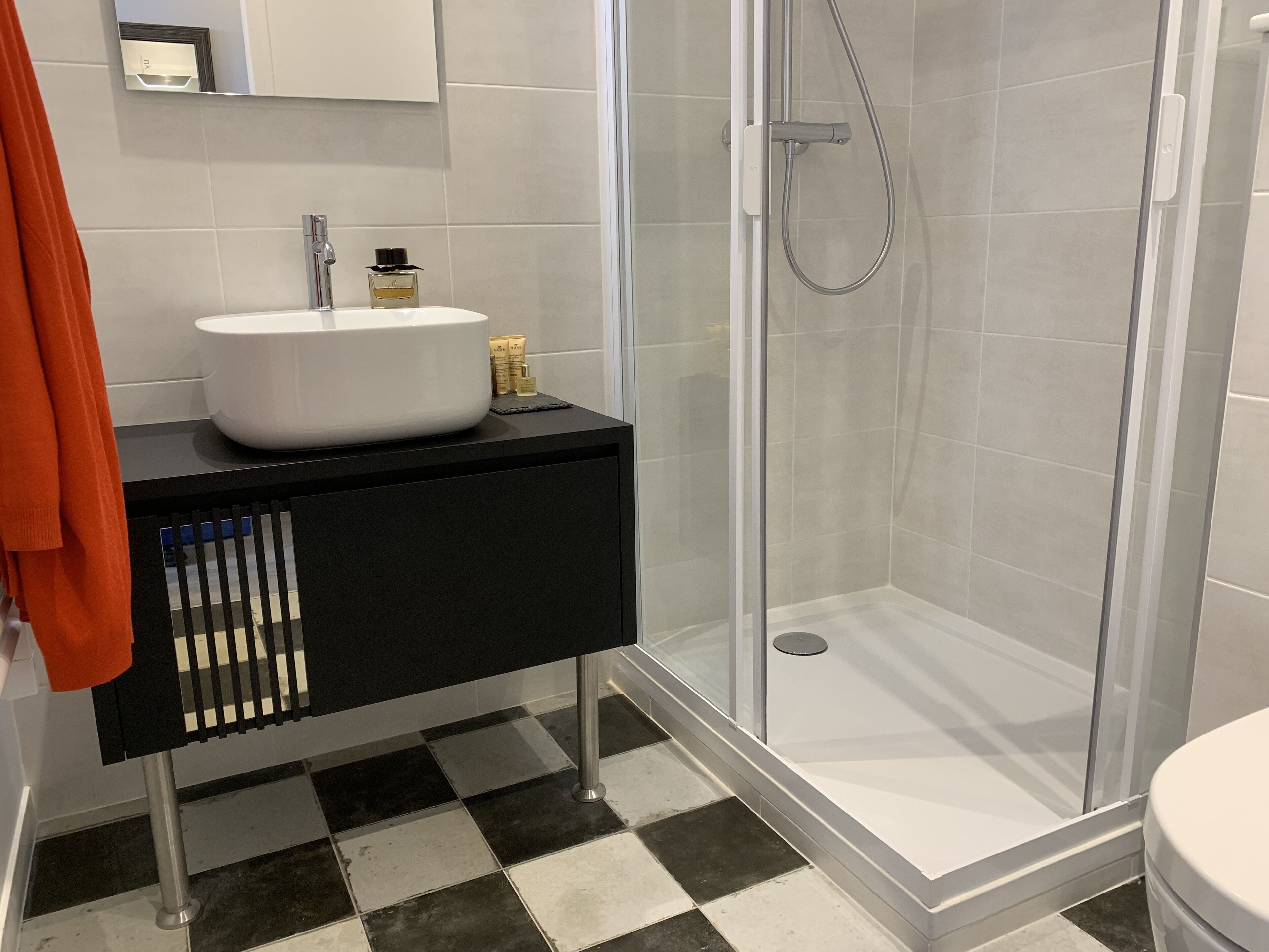 Un bany amb terra de pissos negres i blancs, un rentapeus blanc i una cabina de dutxa de vidre.