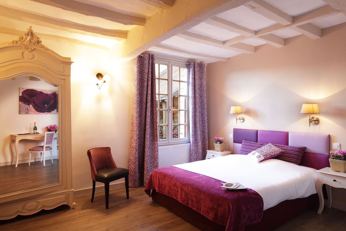 A bedroom with a large bed, a chair, a desk, and a mirror.