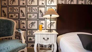 Une chambre d’hôtel comprenant un lit, une chaise, une table de chevet avec une lampe, et un mur décoré d’illustrations d’animaux encadrées.