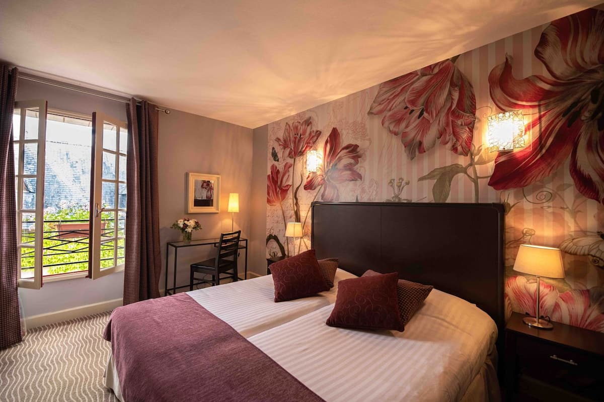 A hotel room with a bed, a desk, a chair, and a view of greenery through a window.