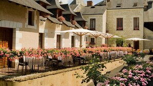 A courtyard with outdoor seating, stone buildings, and flowering plants. - Hostellerie La Croix Blanche (Fontevraud-l'Abbaye)
