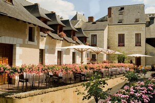 A courtyard with outdoor seating, stone buildings, and flowering plants.