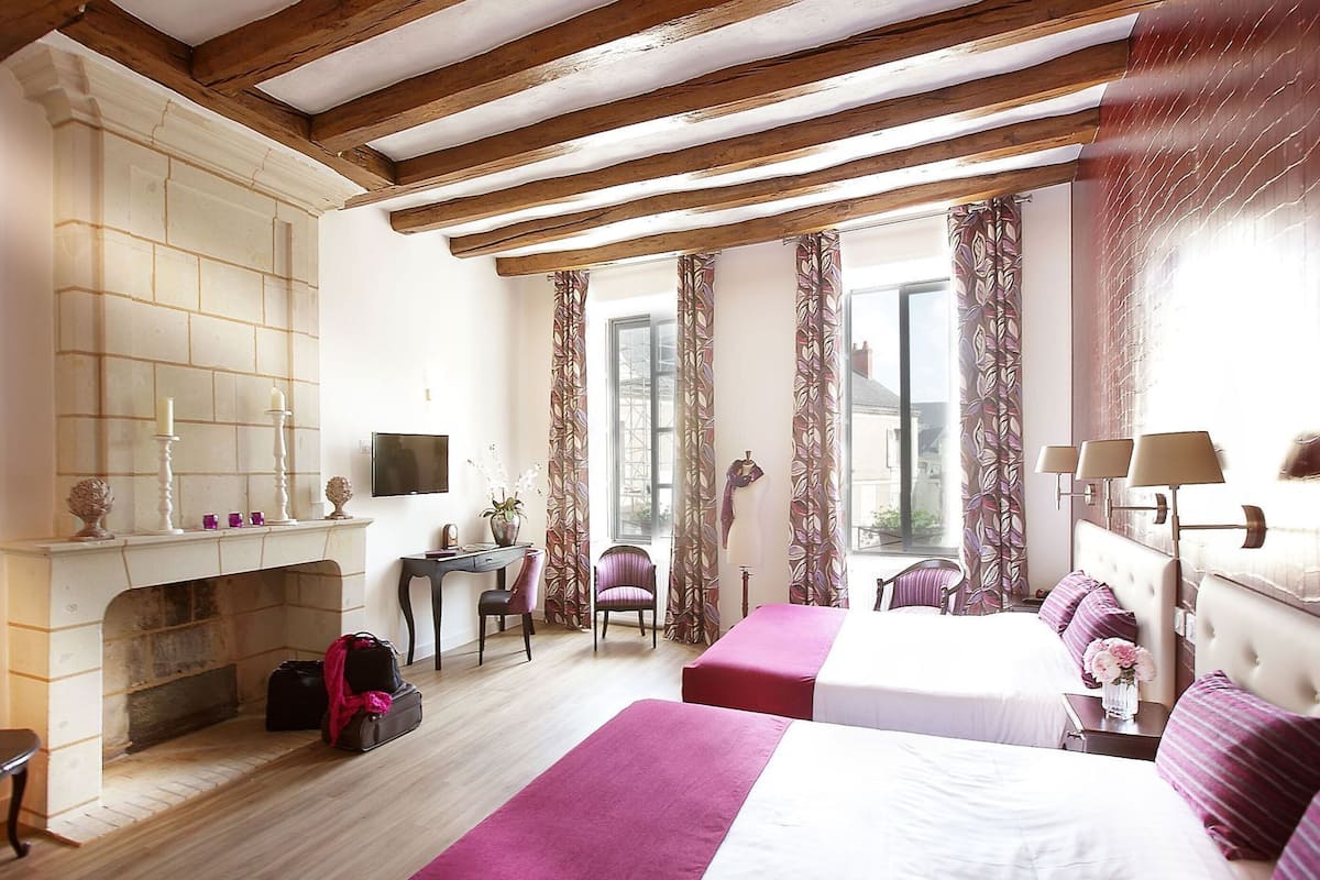 A hotel room with a fireplace, two beds, a desk, and a view of the outside.