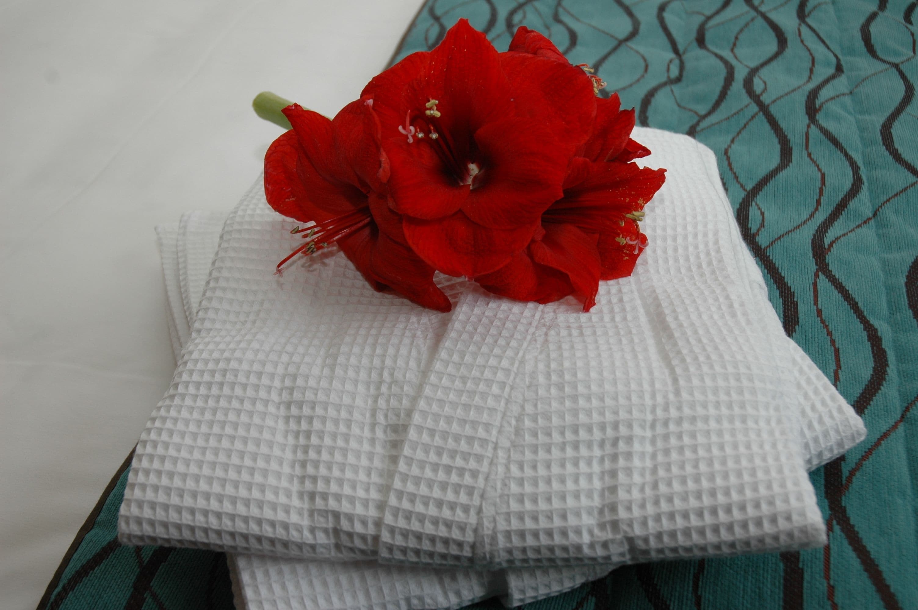 A neatly folded white towel with a red flower placed on top.