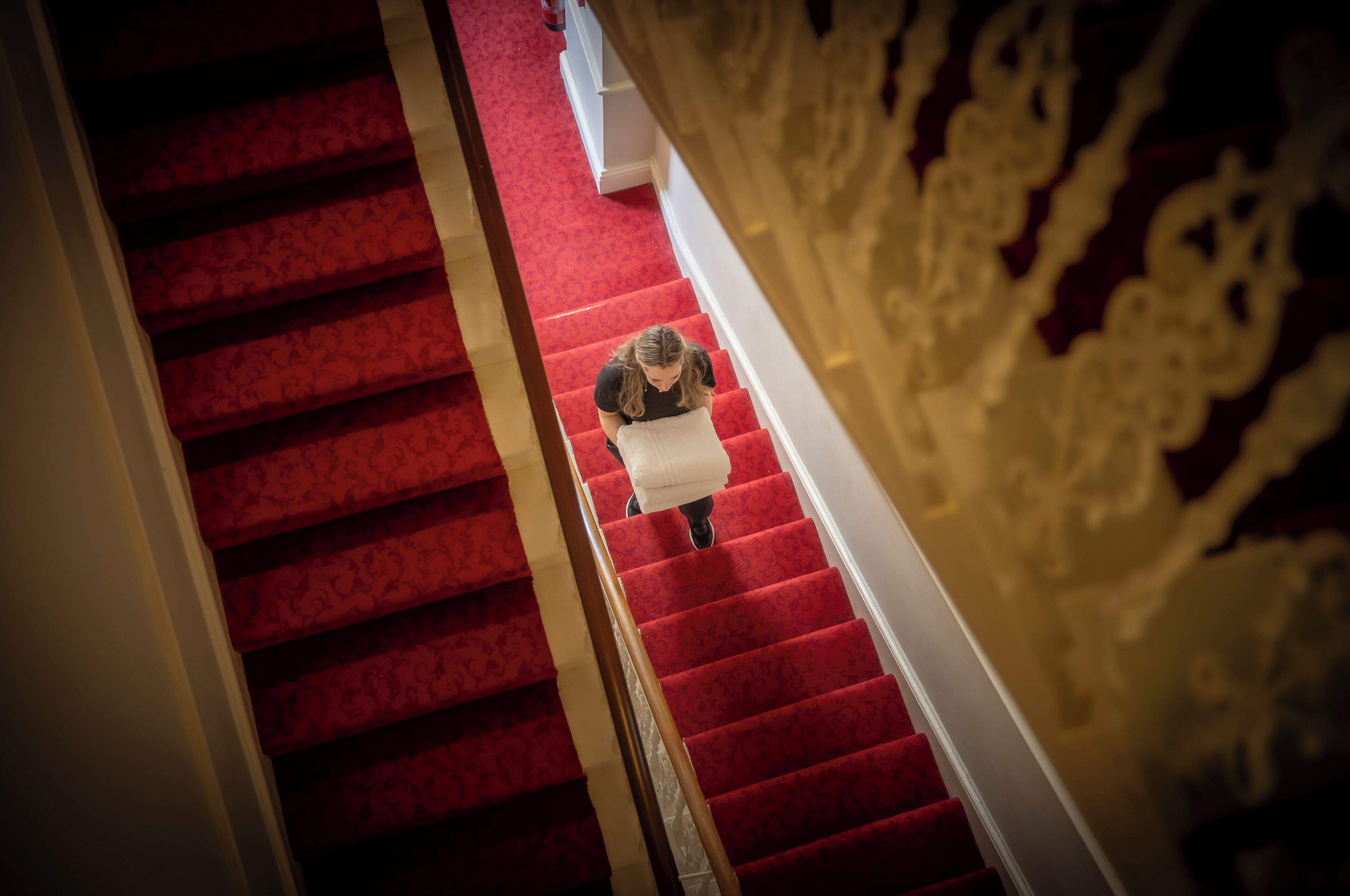Una escalera con peldaños alfombrados de rojo y barandilla blanca.