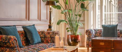 A room with a patterned sofa, a wooden coffee table, a large potted plant, and a vintage dresser.