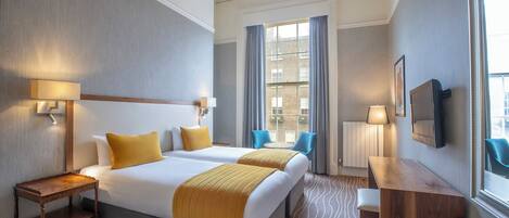 A hotel room with two beds, a desk, a chair, a TV, and a window with curtains.