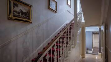 A grand staircase with ornate white balustrades and red carpeted steps, leading to a landing with a door.