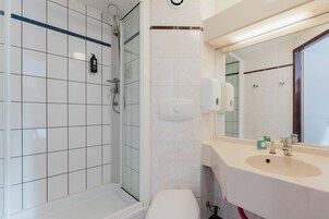 Un baño moderno con cabina de ducha de vidrio, inodoro, lavabo con espejo y dispensador de jabón.